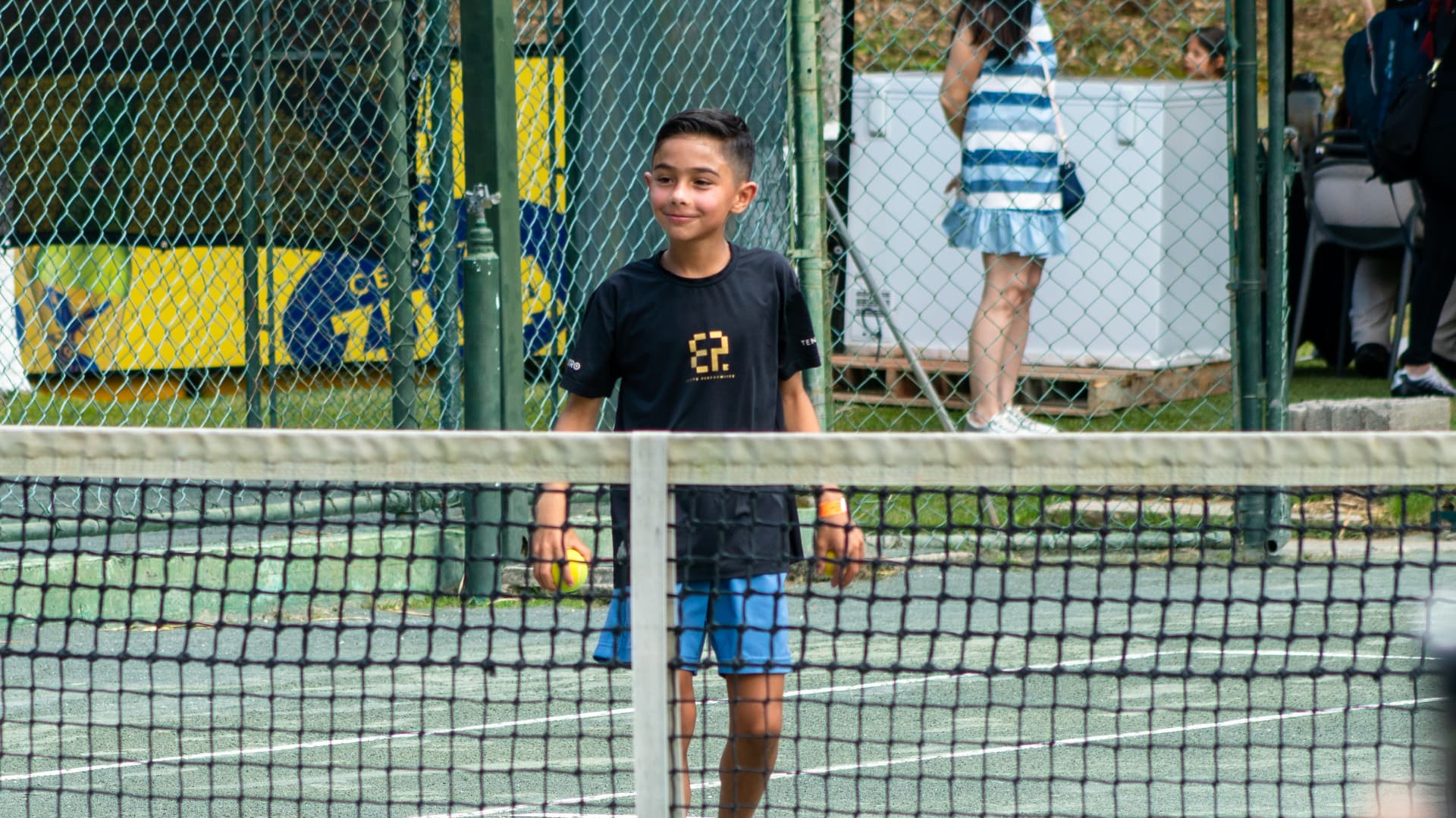 Niño con pelotas de tenis junto a la red